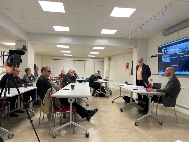 En rum med sittande människor som tittar mot ordföranden.